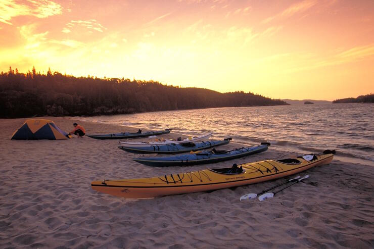 Group of kayaks pulled up on a sandy beach with tent at sunset