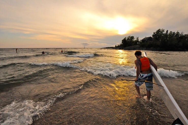 Man with SUP board going into Lake Superior at sunset. 