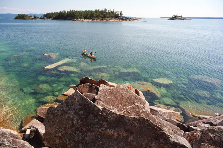 Canoe being paddled along rocky coast of Lake Superior. 