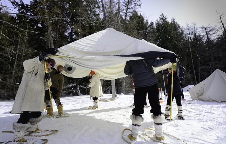 Group of people putting up large white canvas tent