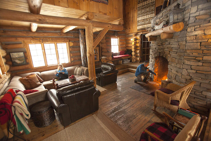 Man stoking a fire and a woman reading in a log cabin