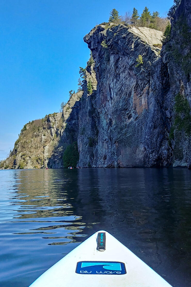 Front end of SUP board on lake looking up a towering cliffs