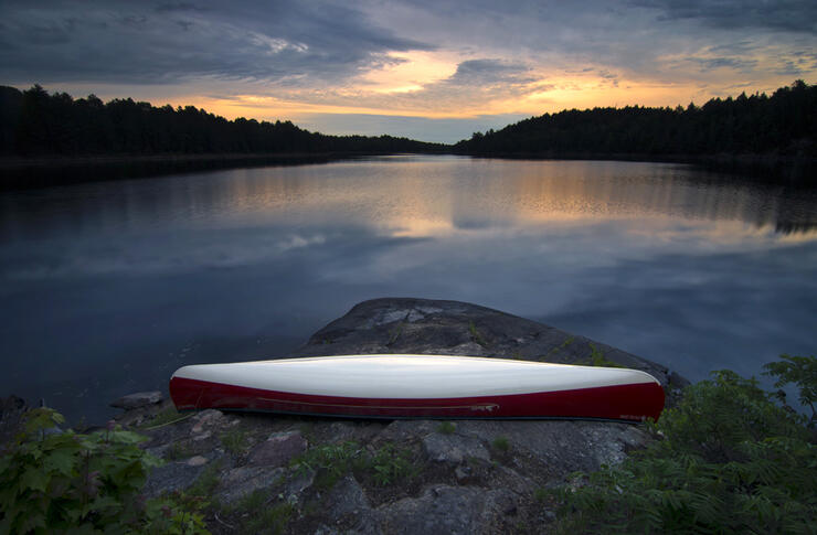 Canoe resting on shore of lake at sunset 
