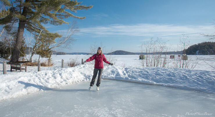 Woman skating on outdoor rink beside a lake.