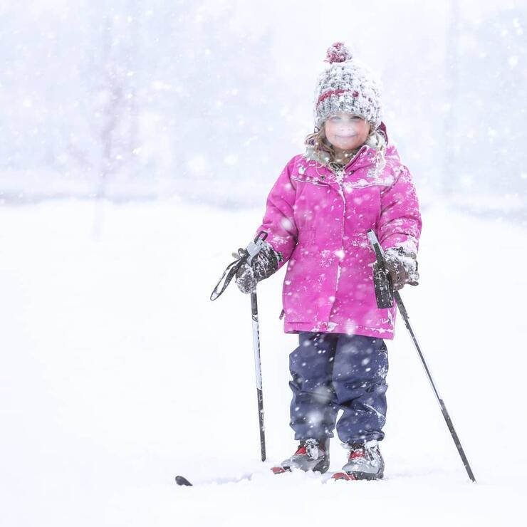 Young girl in pink jacket cross country skiing.in snow storm. 