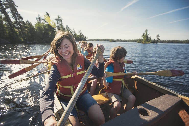 Smiling people paddling a voyageur canoe. 