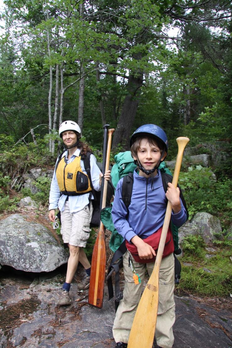 Young boy carrying a pack and paddle 