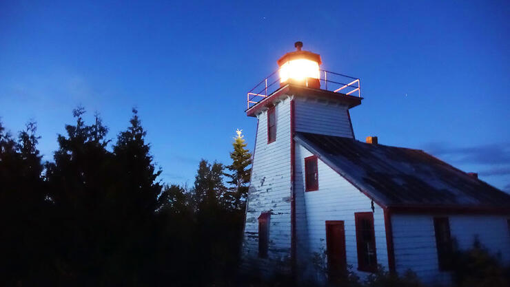 Old wooden lighthouse with light on at night.