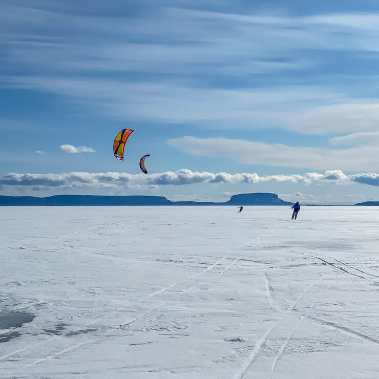 Several snowkiters gliding on a large lake.