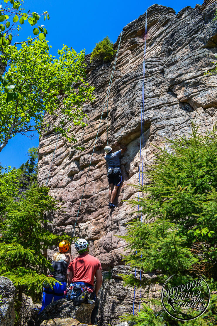 Ropes hanging from top of rock face with a climber ascending. 