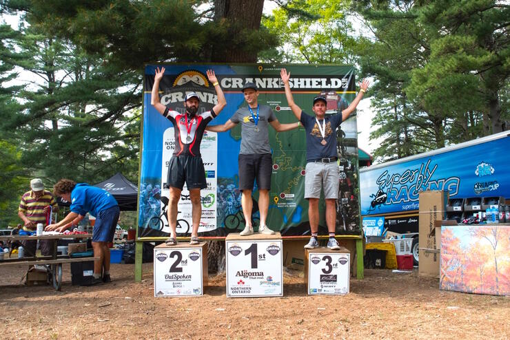 Three winners standing on podiums in forest