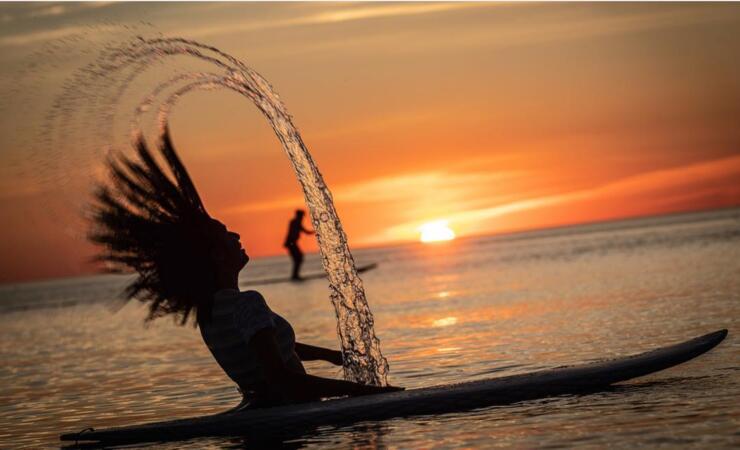 Woman flipping long hair while sitting on a paddleboard at sunset. 