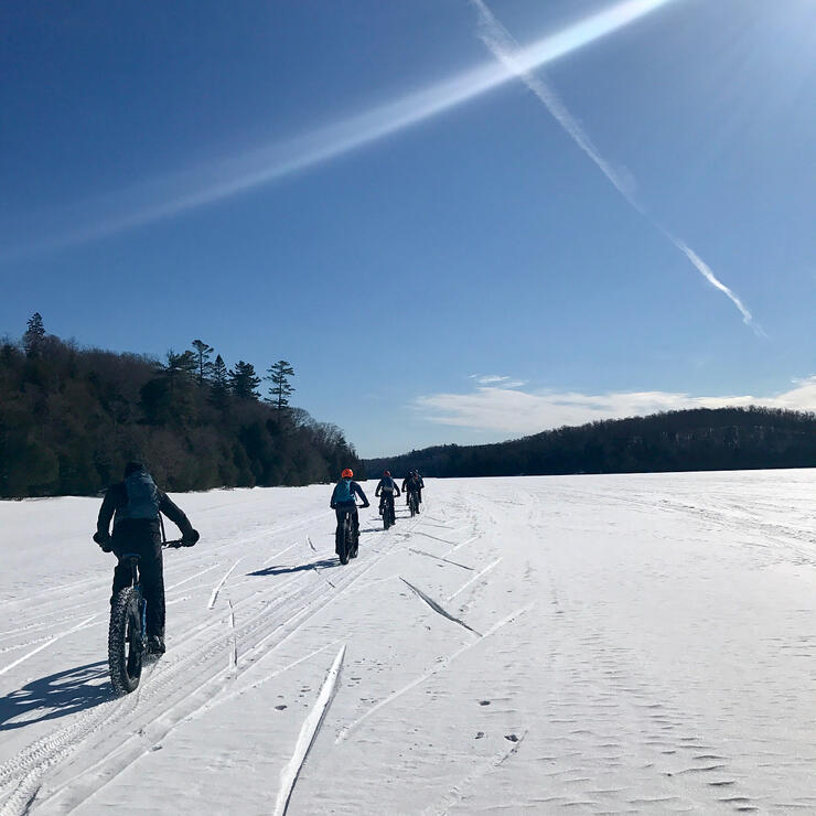 A group of fat bikers riding on a frozen  lake in single file. 