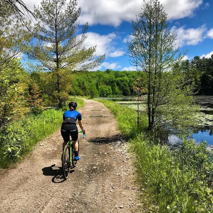 Woman riding a bicycle on a gravel road beside a pond