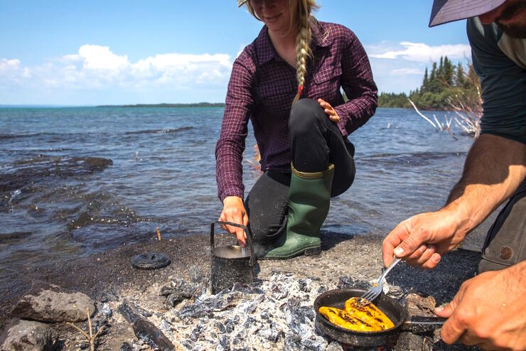 Man and woman cooking fish in a frypan over an open fire