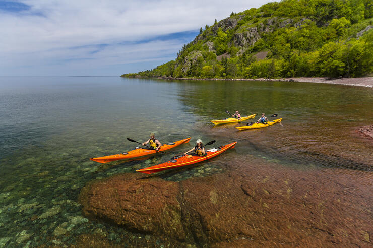 Four kayakers paddling over crystal clear water along rocky coast