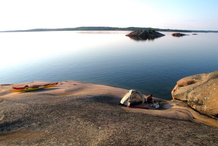 Tent and kayak on a smooth rocky shoreline. 