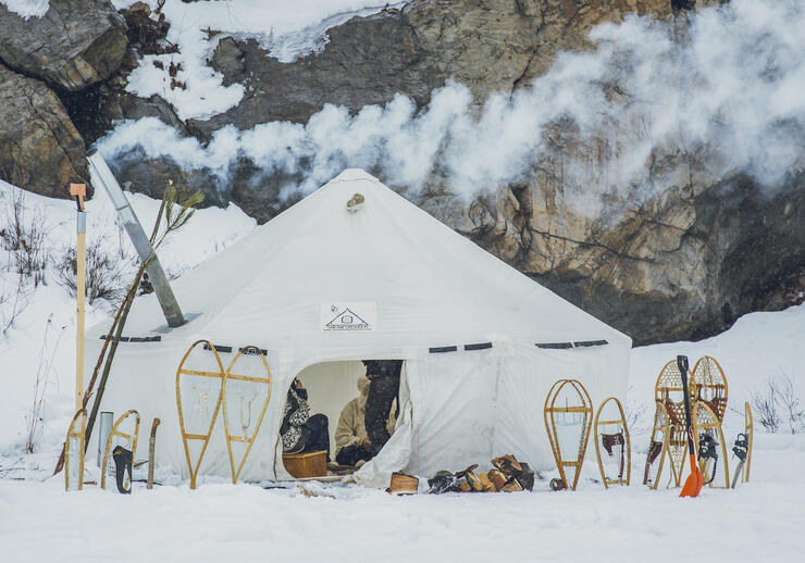 Large white canvas tent with smoke coming out chimney, snowshoes standing in snow