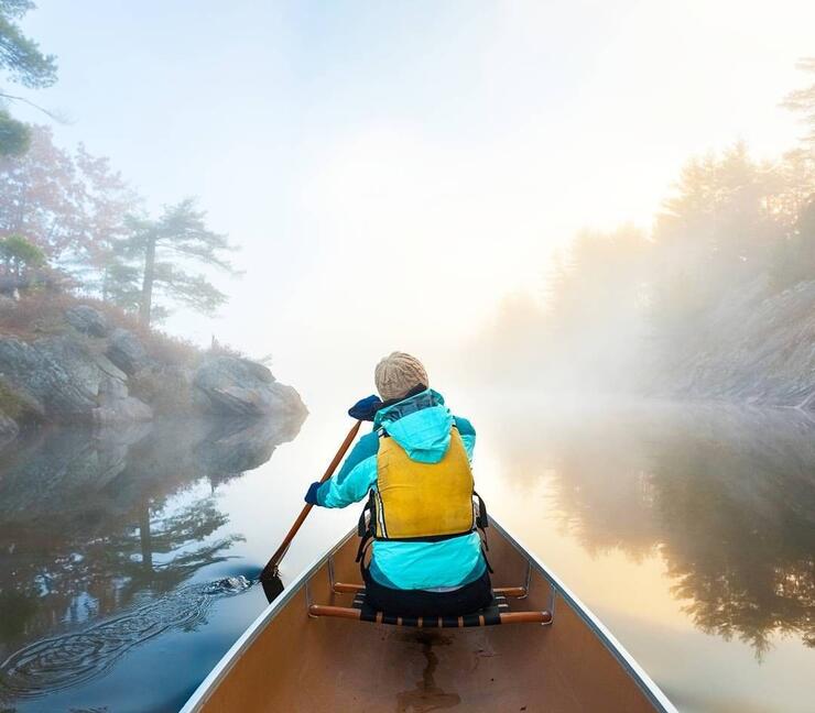 Person wearing a jacket and life jacket paddling in bow of a canoe. 