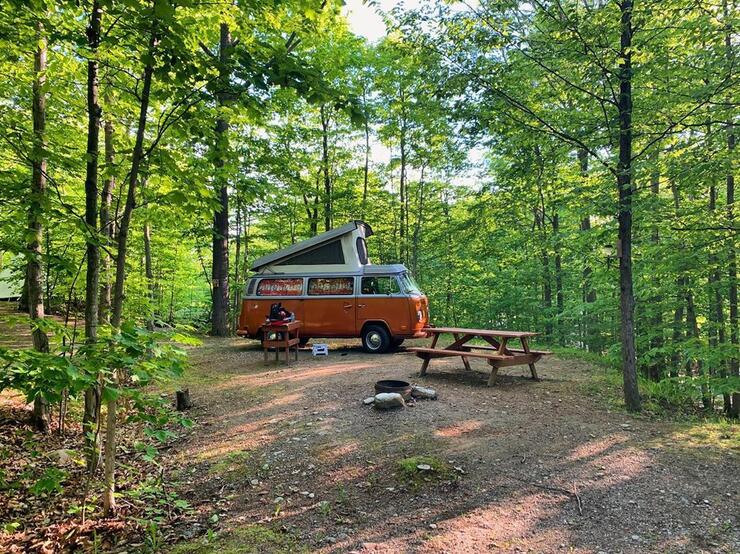 An orange and white camper van parked beside a picnic table. 
