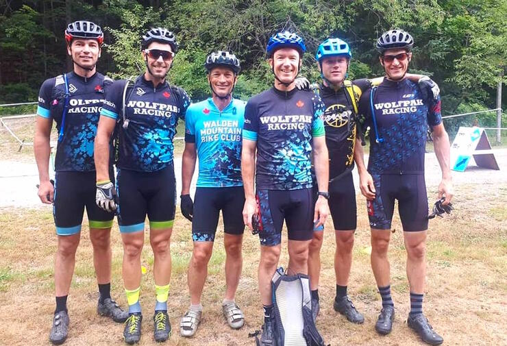 Group of men standing together. All wearing same shirt and bicycle helments. 