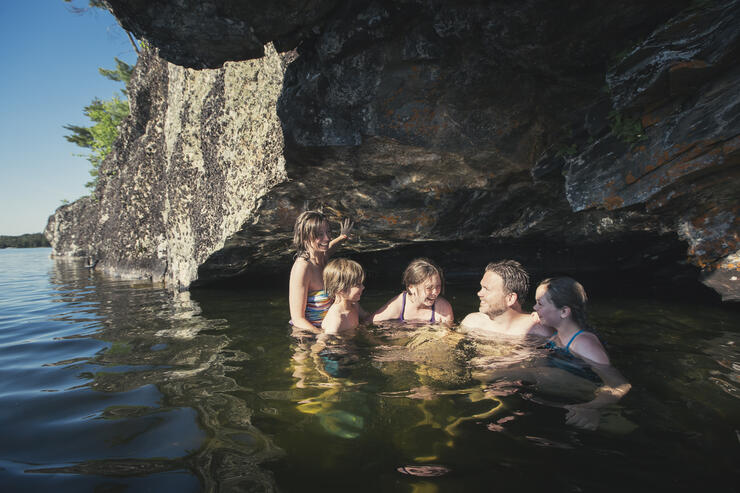 Man, woman and three children swimming under a rocky outcrop. 