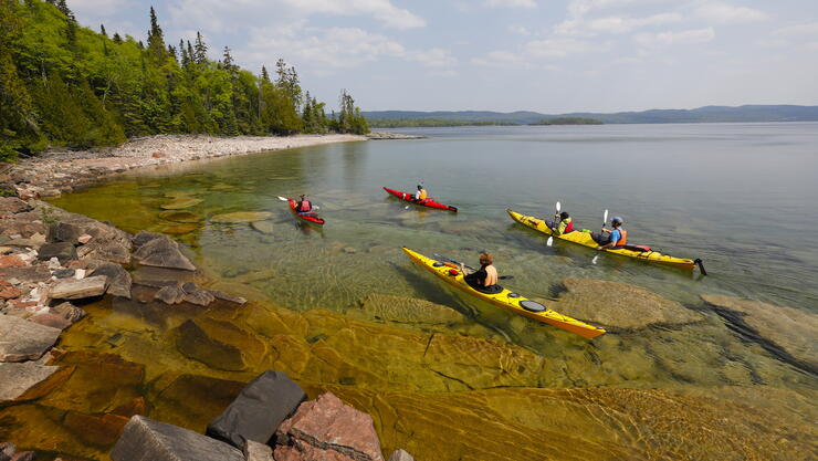 A group of kayakers paddling clear waters along Lake Superior coast. 