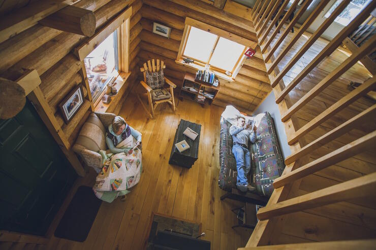 Looking down from a loft at two people relaxing in a cozy log cabin.