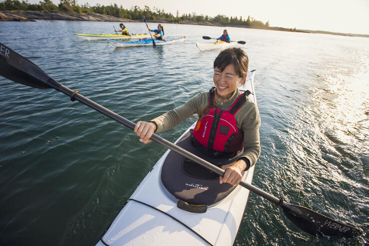 Close-up of a woman paddling a kayak on Georgian Bay with three other women kayakers.