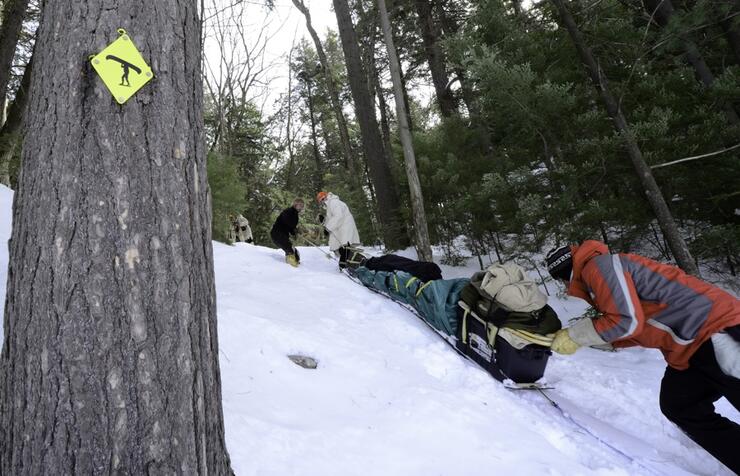 Man pushed loaded toboggan up a snow-covered hill beside tree with portage sign