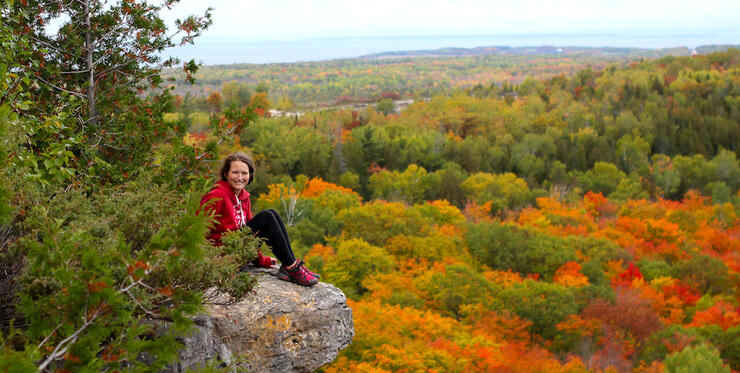 Woman sitting on a rock ledge overlooking scenic fall foliage 