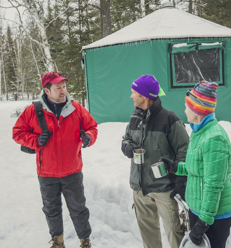 Three people talking outside a green yurt in winter.
