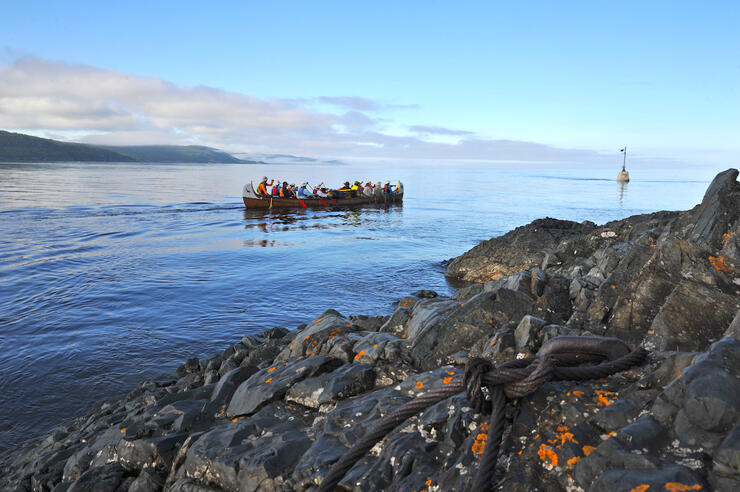 Voyageur canoe paddling along shoreline 
