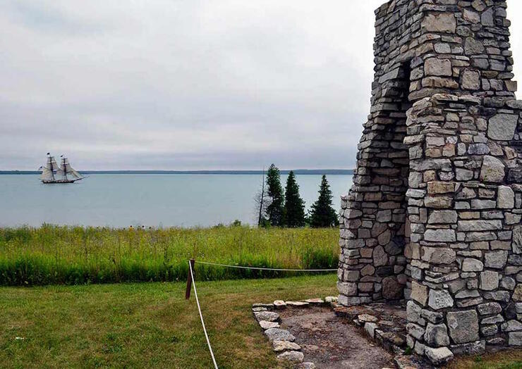 Stone monument on grass with a schooner sailing in background