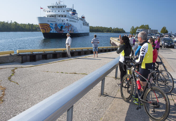 Group of cyclists watching a large passenger ferry arriving at a dock.