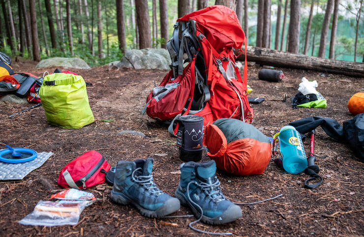 Boots, plates, pack, dry bags and other gear on a campsite.