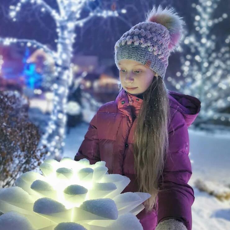 Young girl in winter jacket and hat looking at glowing lights. 