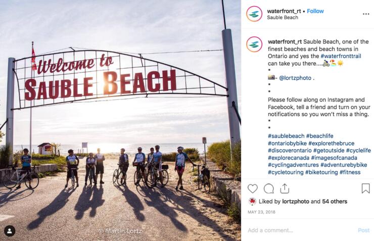 Instagram post showing cyclists under the Welcome to Sauble Beach sign