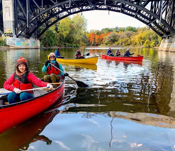 Three canoes paddling under a metal bridge arch.