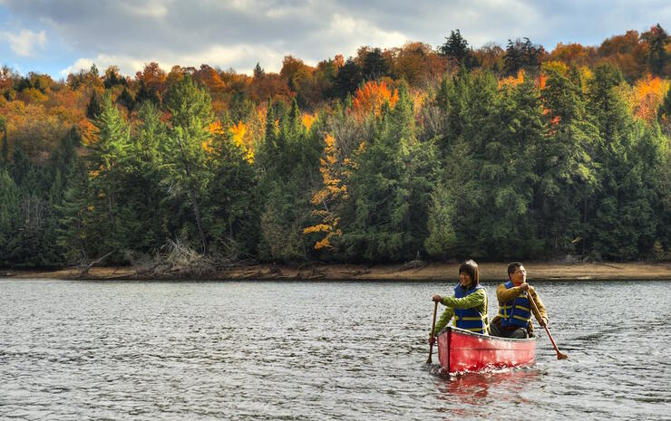 Two people paddling a red canoe with autumn colours in background