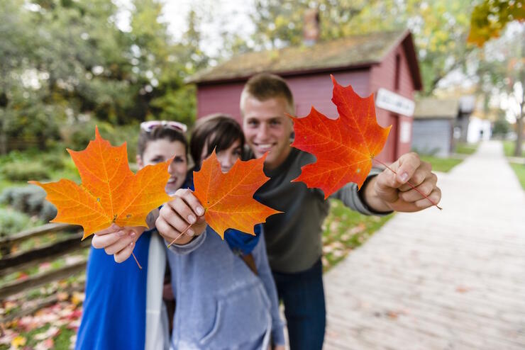 Three kids holding colourful maple leaves. 