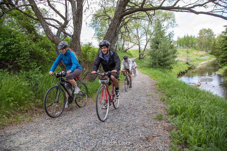 Cyclists riding on a gravel path beside a river. 