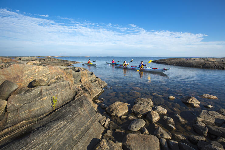 Three kayakers paddling through a sheltered bay surrounded by smooth rock.