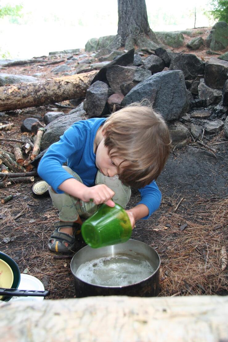 Young boy washing dishes at a campsite