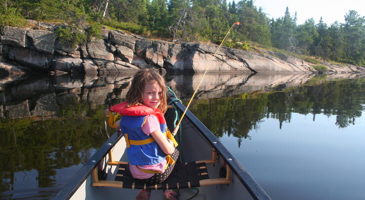 Young girl in canoe fishing on a calm river. 