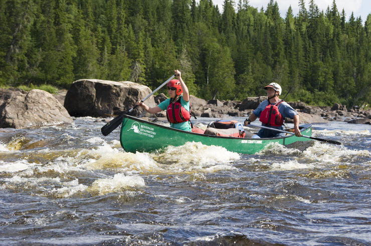 Two people paddling a green canoe on a whitewater river.