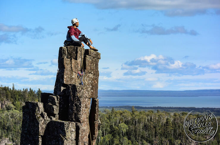Man sitting on top of a very tall rock pillar. 