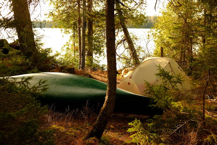 Green canoe resting on lakeside campsite with tent