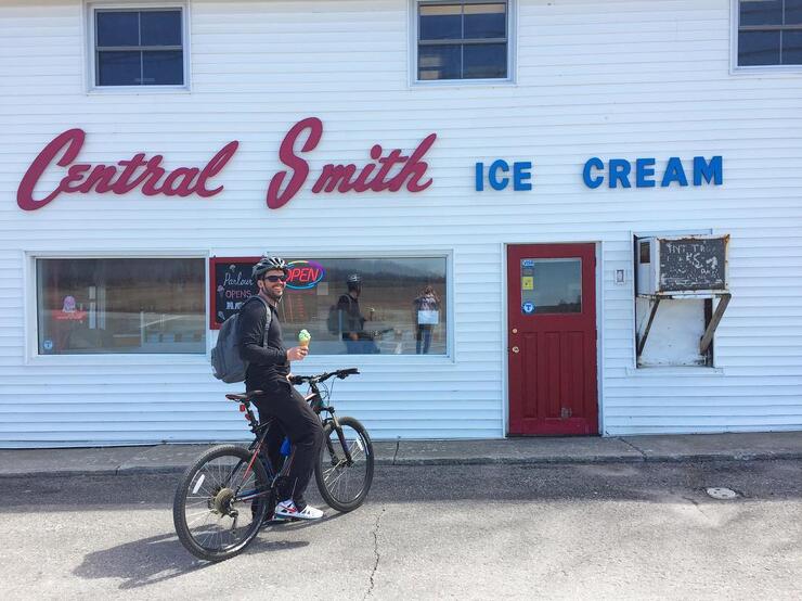 Man on a bicycle eating an ice cream in front of Central Smith Ice Cream. 