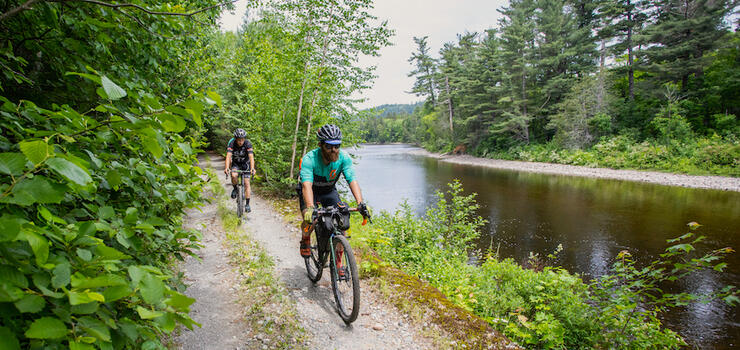 Two cyclists riding a gravel road beside a river